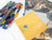 Collection of colorful art pieces and a yellow sheet with 'Dazzledots' branding on a white surface.
