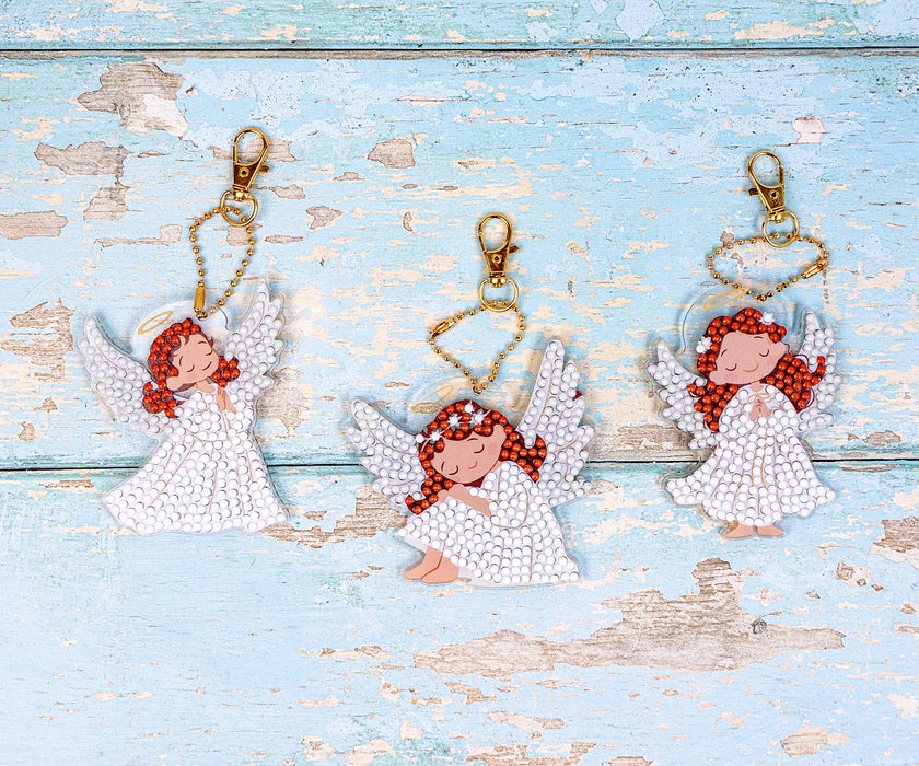 Three angel keychains with red hair on a light blue wooden background