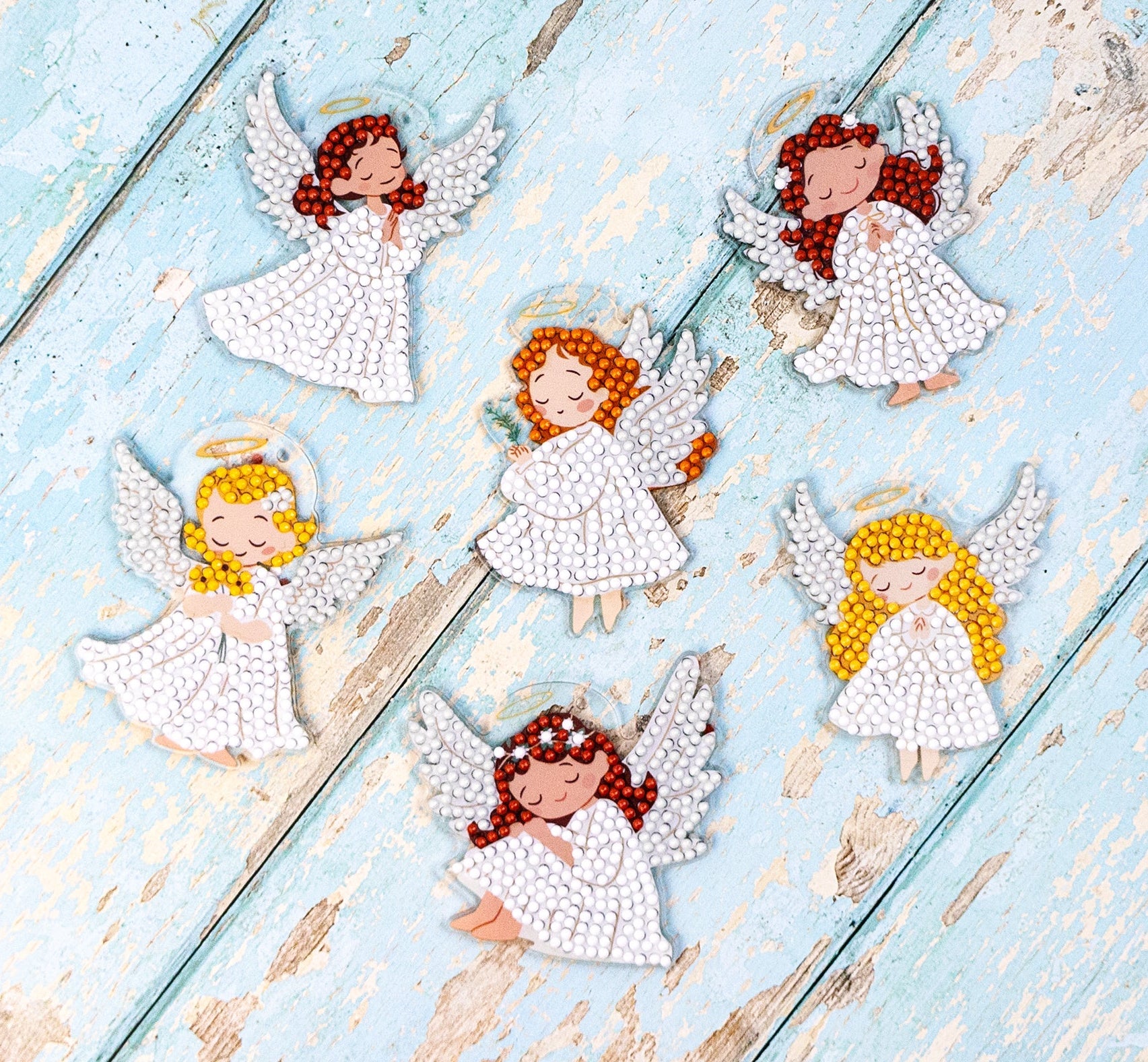 Decorative angel figurines with red hair on a light blue wooden surface