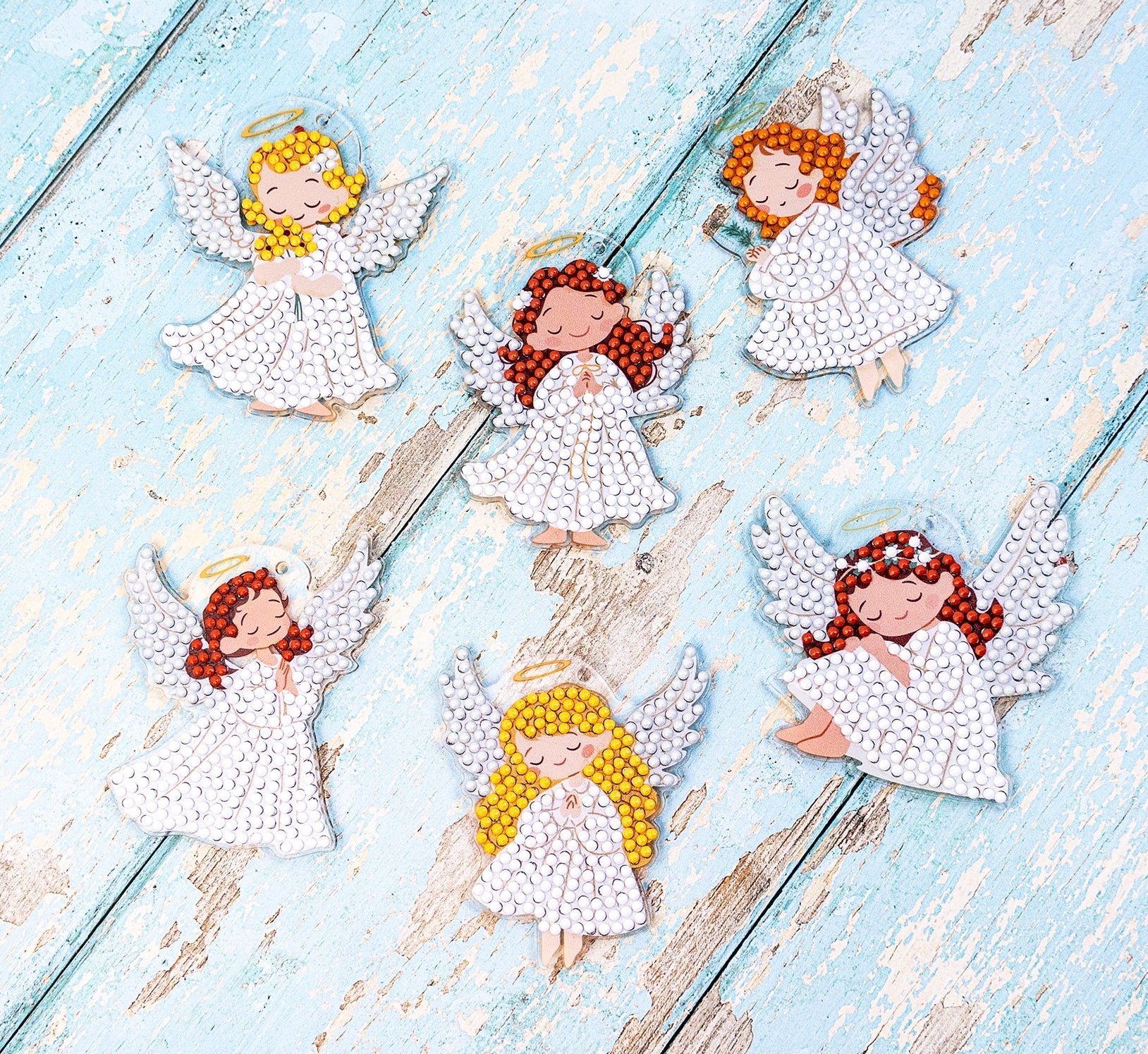 Decorative angel figurines with red hair and yellow hair on a light blue wooden surface.