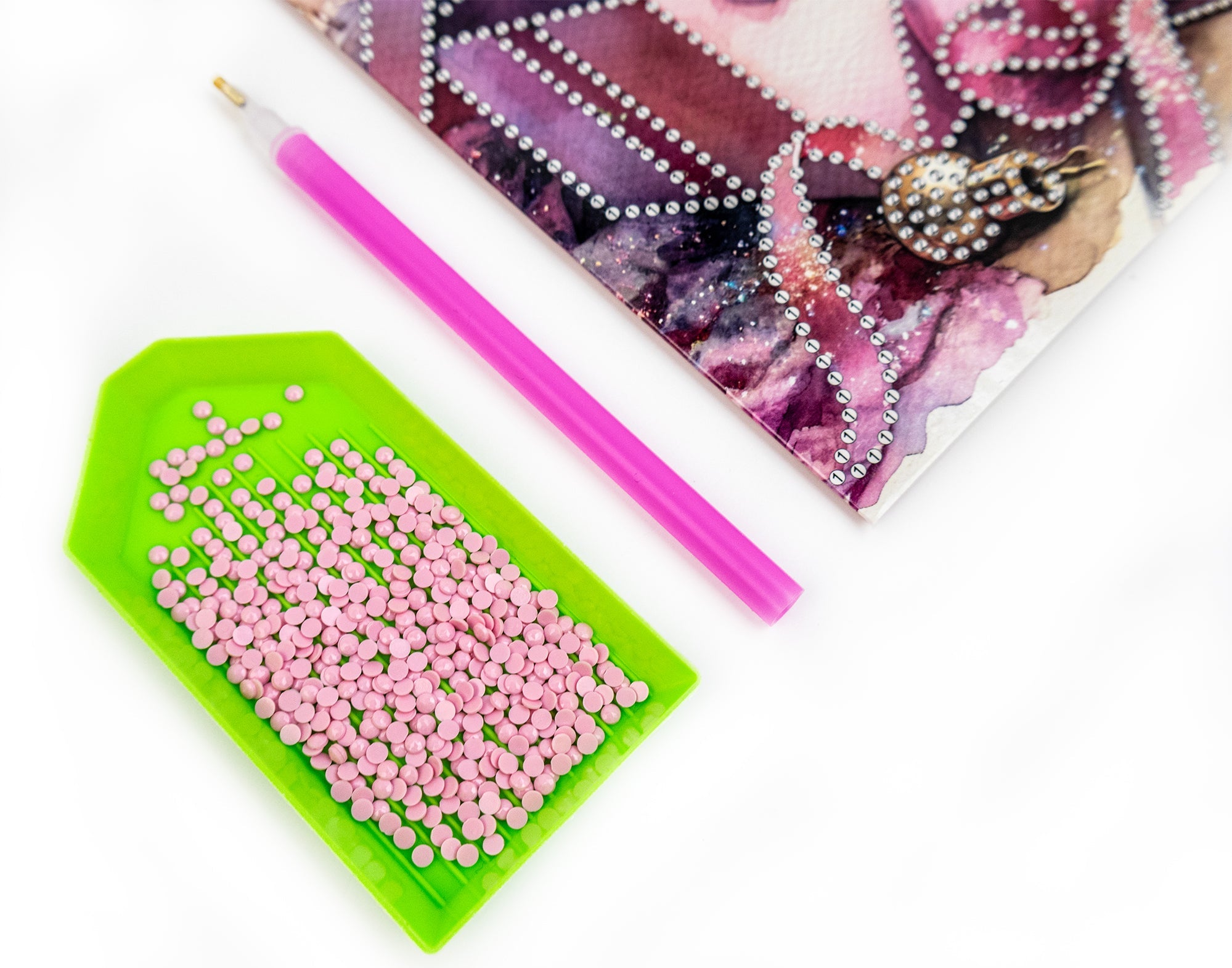 Green tool with pink beads, pink straw, and decorative item on a white background