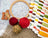 Embroidery hoop with cross-stitch pattern, red yarn, wooden beads, and thread spools on a textured surface.