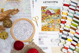 Embroidery hoop, threads, scissors, and a pattern book on a table with a Letistitch brand label.