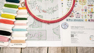 Embroidery hoop with colorful threads and a pattern sheet on a wooden surface