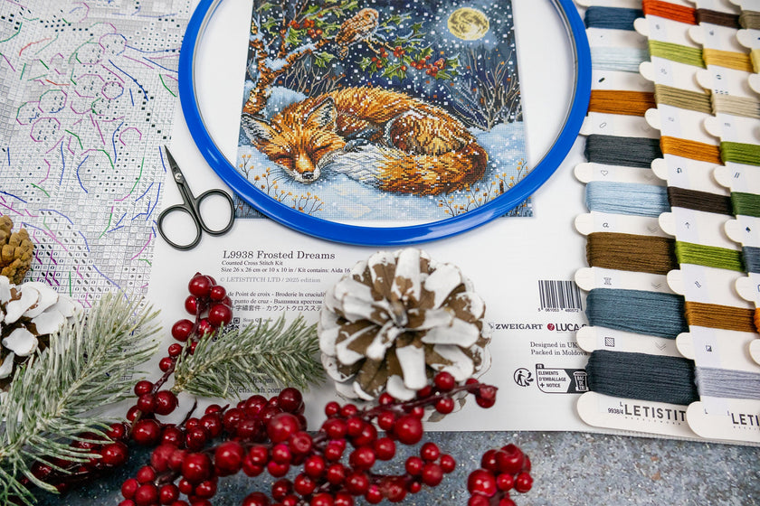 Embroidery hoop with a fox design, scissors, thread spools, and decorative items on a table.