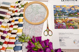 Embroidery hoop with cross-stitch pattern, scissors, and color swatch on a table.