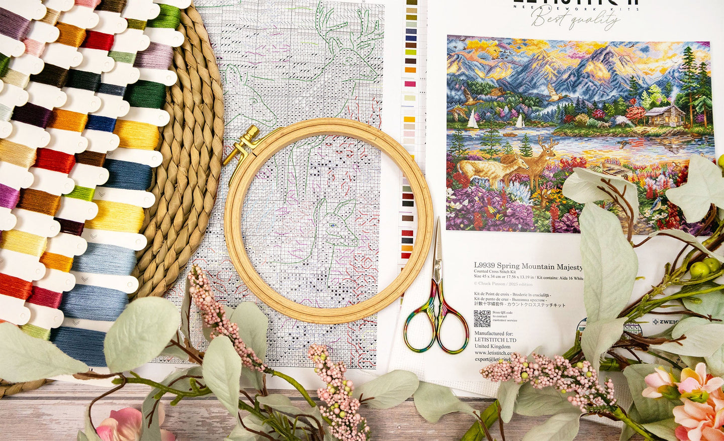 Embroidery hoop with colorful threads, scissors, and a scenic painting on a wooden surface.