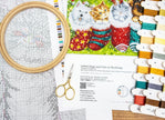 Embroidery kit with cross-stitch pattern, threads, scissors, and a printed design of dogs and cats in stockings.