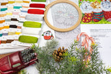 Cross-stitching materials including a hoop, threads, and a partially completed cross-stitch design on a festive-themed fabric.