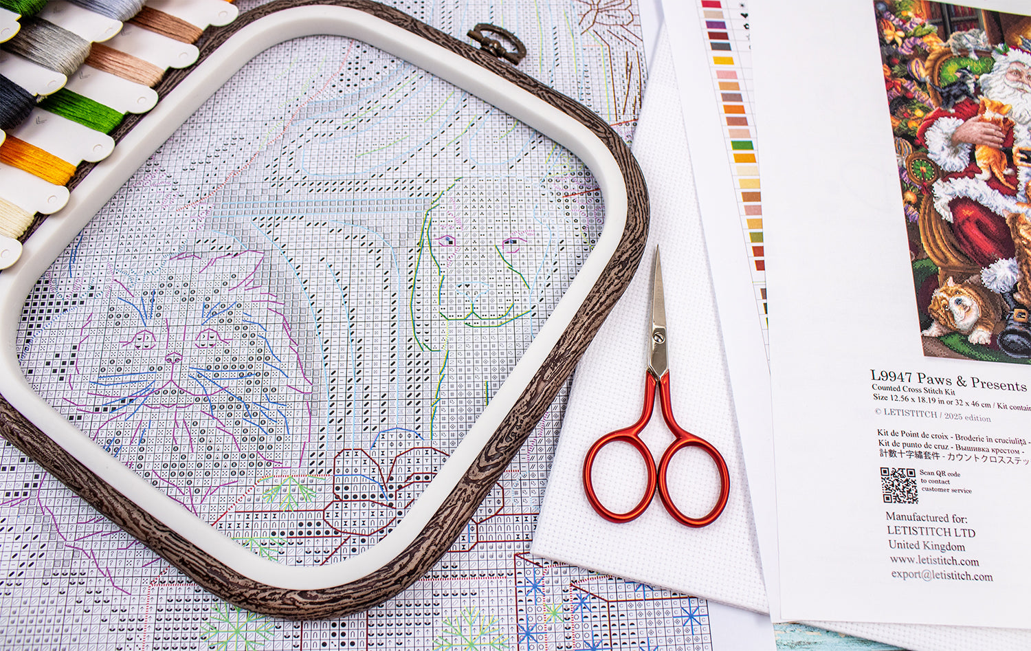 Embroidery hoop with cross-stitch pattern, scissors, and color chart on a table.
