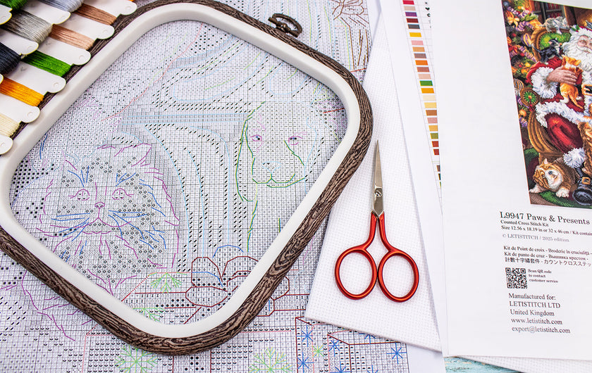 Embroidery hoop with cross-stitch pattern, scissors, and color chart on a table.
