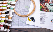 Embroidery hoop, thread spools, and a pattern sheet on a wooden surface.