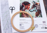 Embroidery hoop with cross-stitch pattern of a woman and wolf on a flat surface.