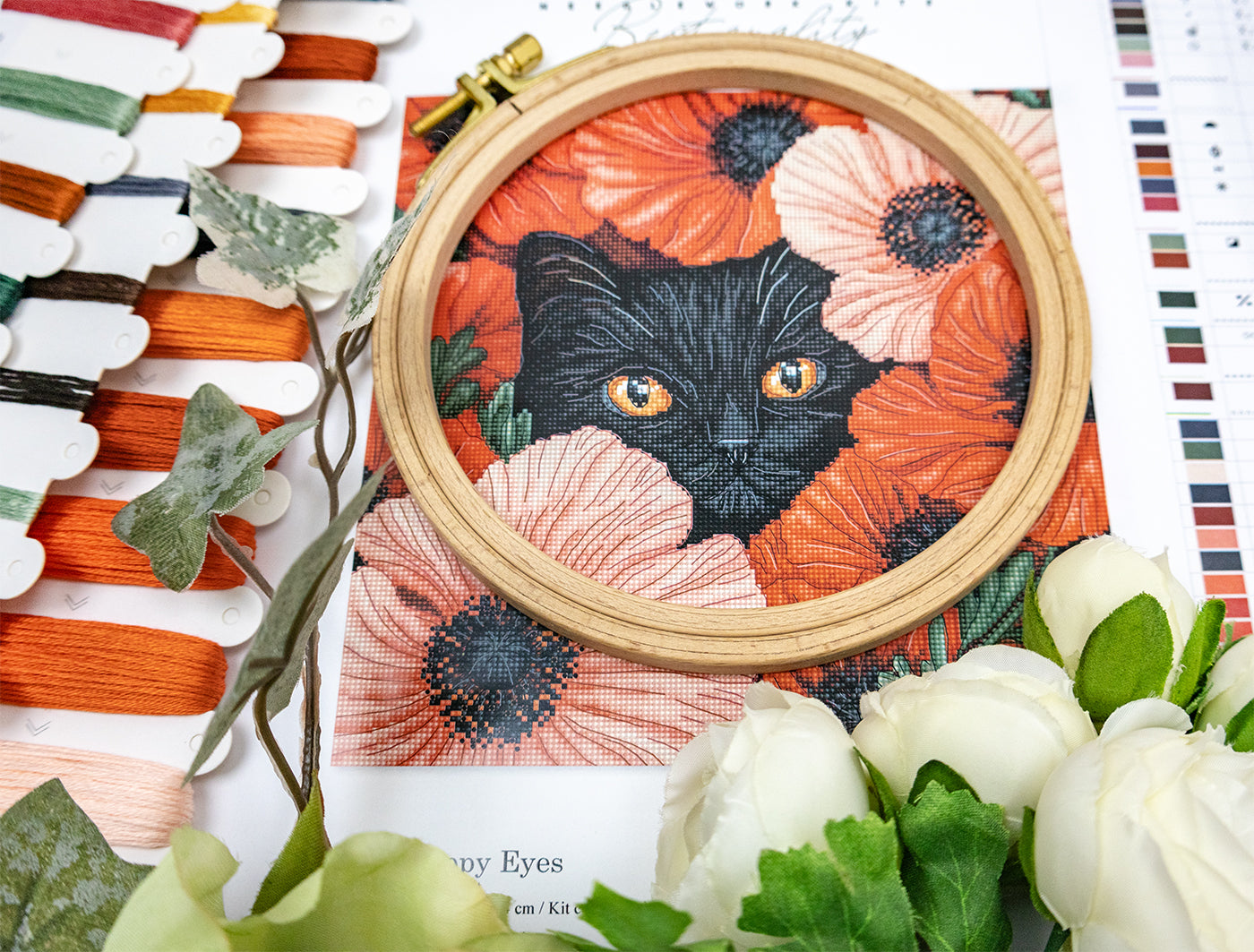 Embroidery hoop with a black cat surrounded by flowers on a floral-patterned fabric background.
