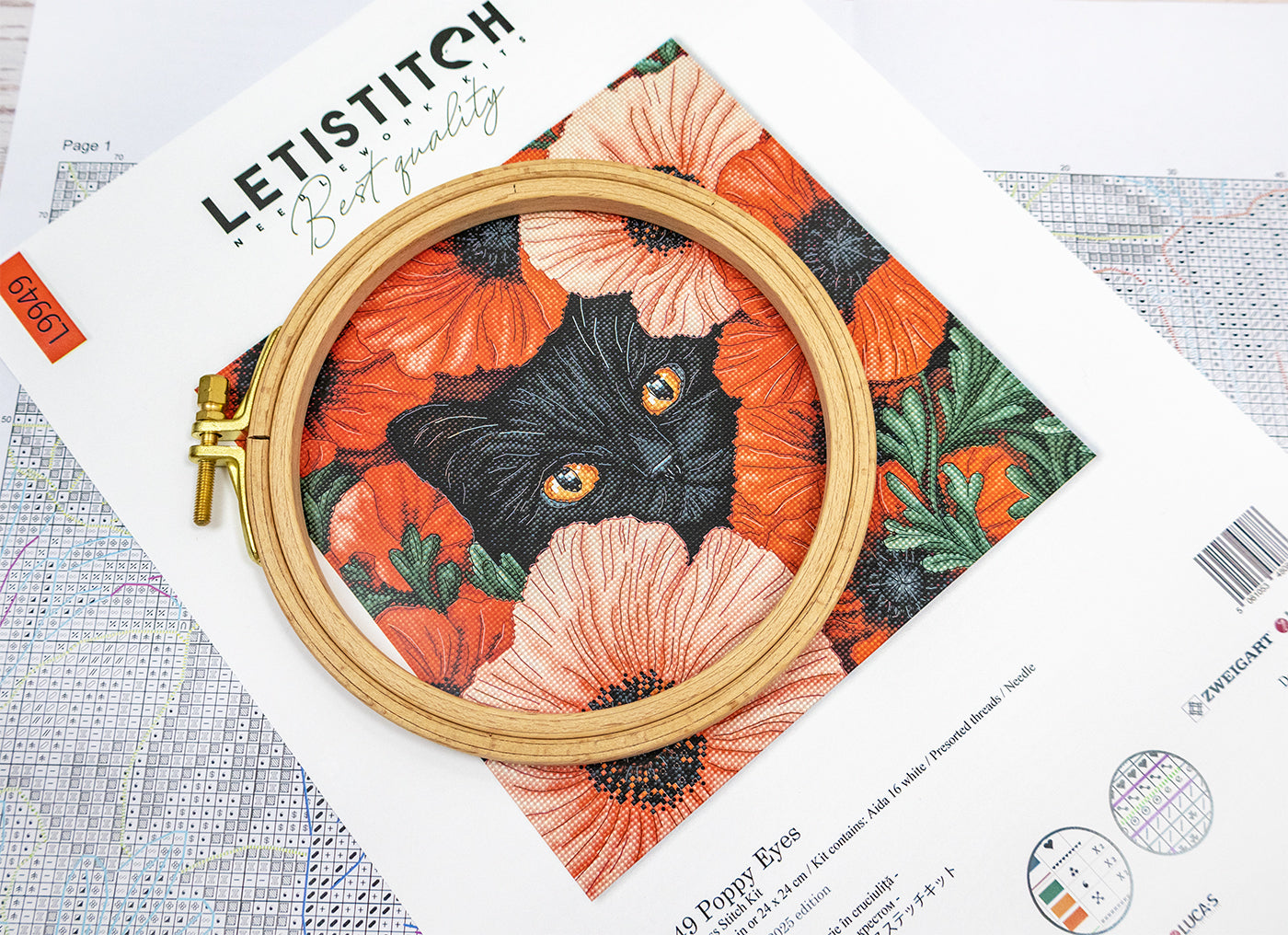 Embroidery hoop with a black cat design on floral fabric, placed on a Letistitch embroidery kit packaging.