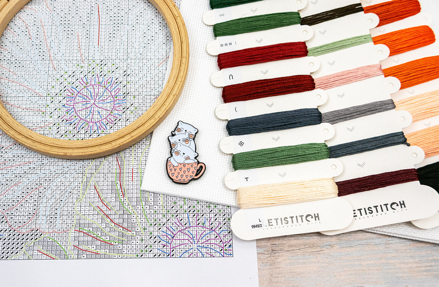 Embroidery hoop with cross-stitched design and color swatches labeled 'ETISTITCH' on a wooden surface.