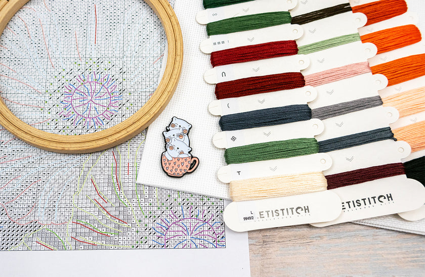 Embroidery hoop with cross-stitched design and color swatches labeled 'ETISTITCH' on a wooden surface.