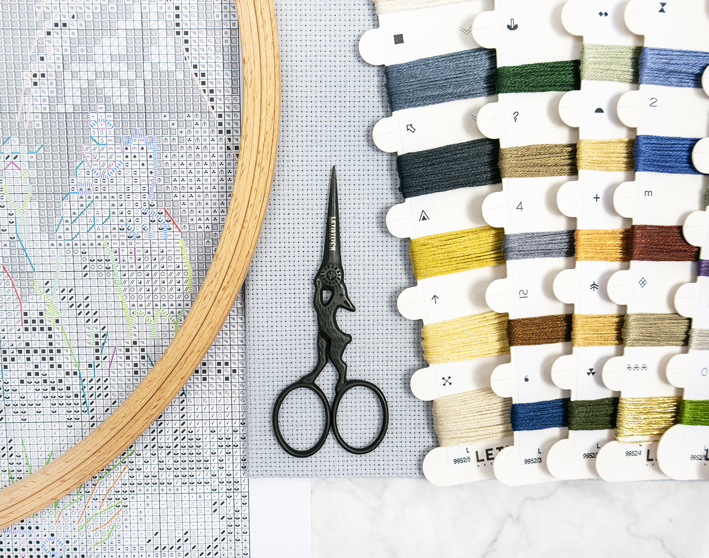 Embroidery hoop, scissors, and thread spools on a cross-stitching fabric.