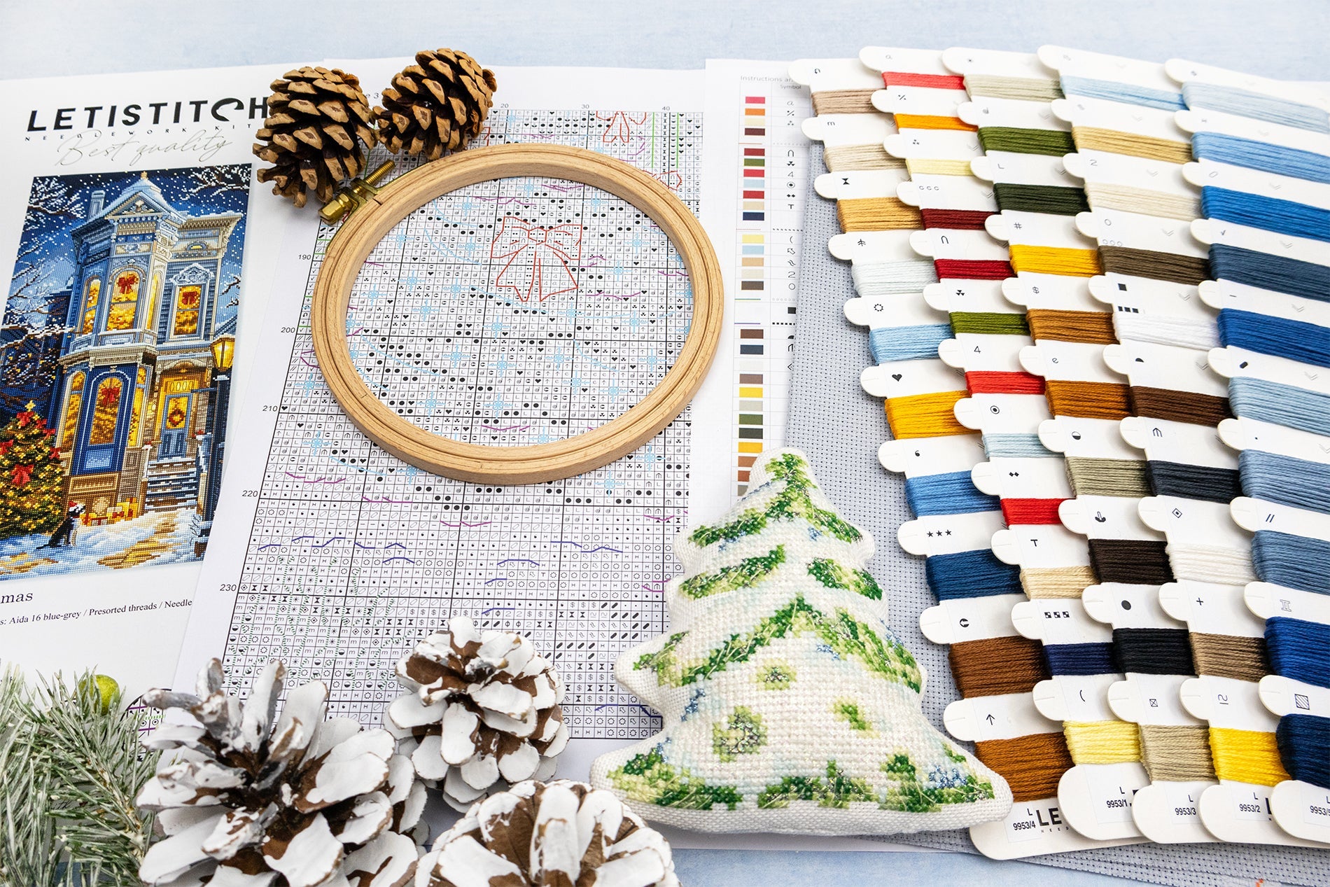 Cross-stitching materials including an embroidery hoop, thread colors, and a Christmas-themed fabric swatch on a light surface.