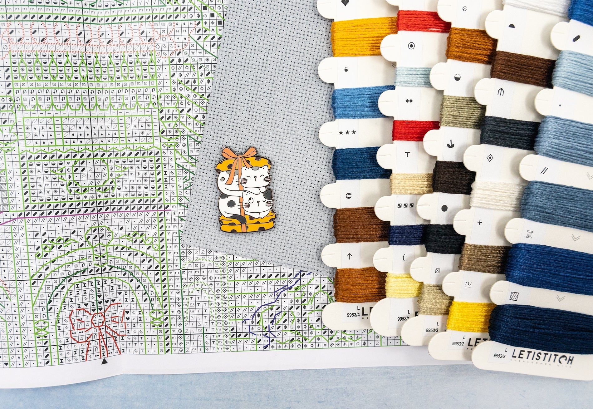 Collection of colorful thread spools and a cross-stitch pattern on fabric.