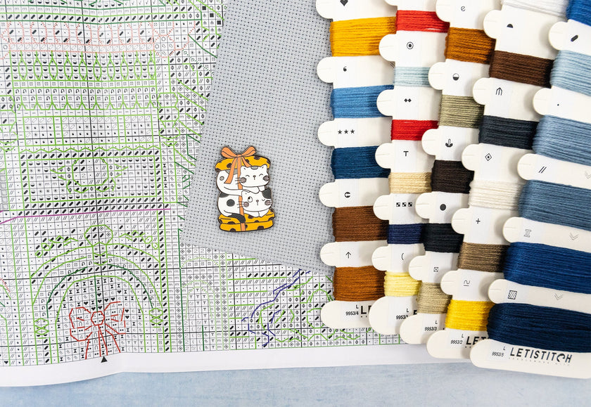 Collection of colorful thread spools and a cross-stitch pattern on fabric.
