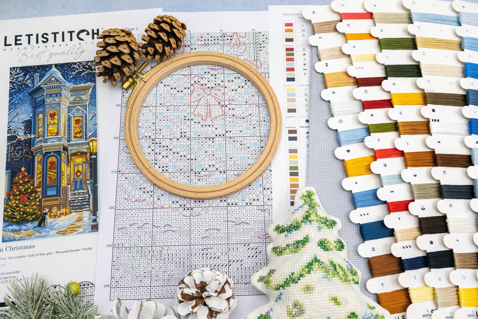 Cross-stitching materials including an embroidery hoop, pattern sheet, and thread selection on a table.