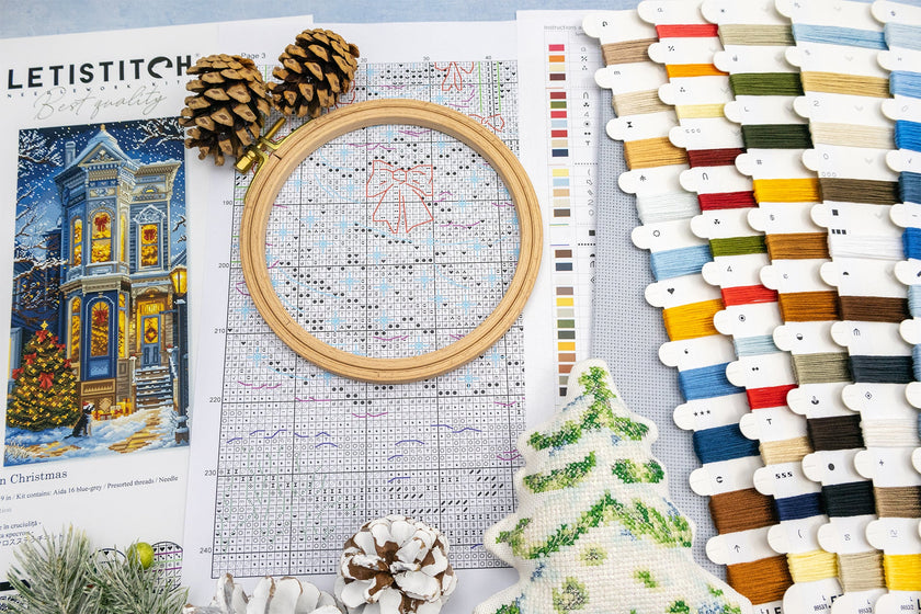 Cross-stitching materials including an embroidery hoop, pattern sheet, and thread selection on a table.
