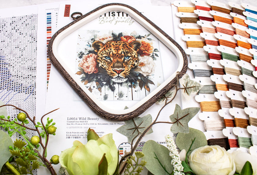 Embroidery hoop with a tiger design surrounded by floral elements and thread spools.