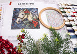 Embroidery hoop with a horse design, fabric, and embroidery thread on a table.