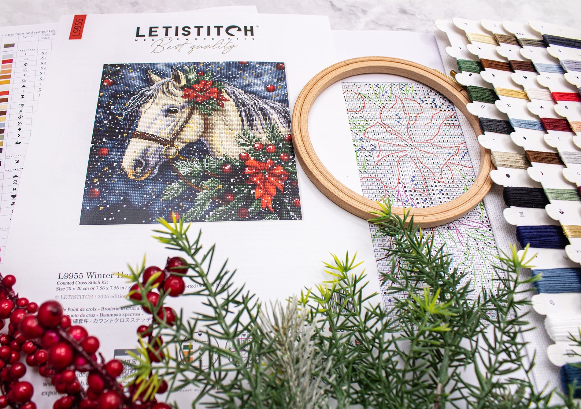 Embroidery hoop with a horse design, fabric, and embroidery thread on a table.