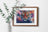 Framed artwork of a tiger with floral background on a white wall with green leaves.