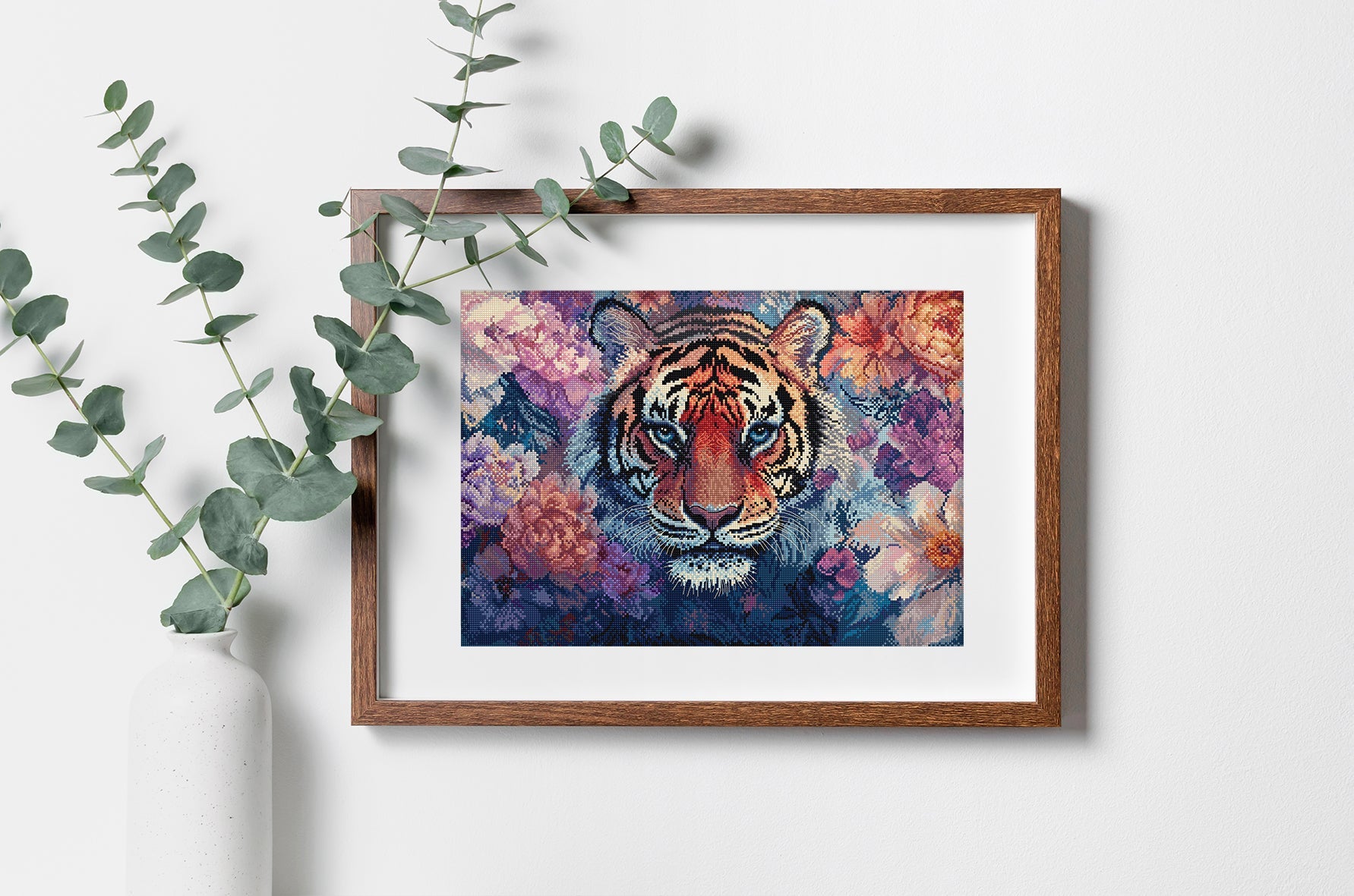 Framed artwork of a tiger with floral background on a white wall with green leaves.