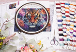 Embroidery hoop with a tiger design surrounded by thread spools and scissors on a magazine page.