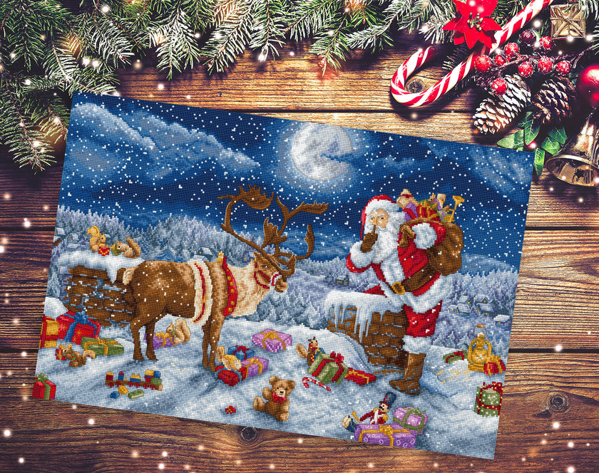 Decorative Christmas scene with Santa Claus, reindeer, and gifts on a wooden surface.