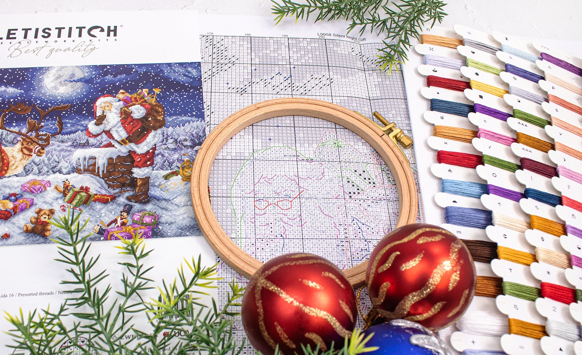 Embroidery hoop, cross-stitch pattern, and Christmas ornaments on a table.