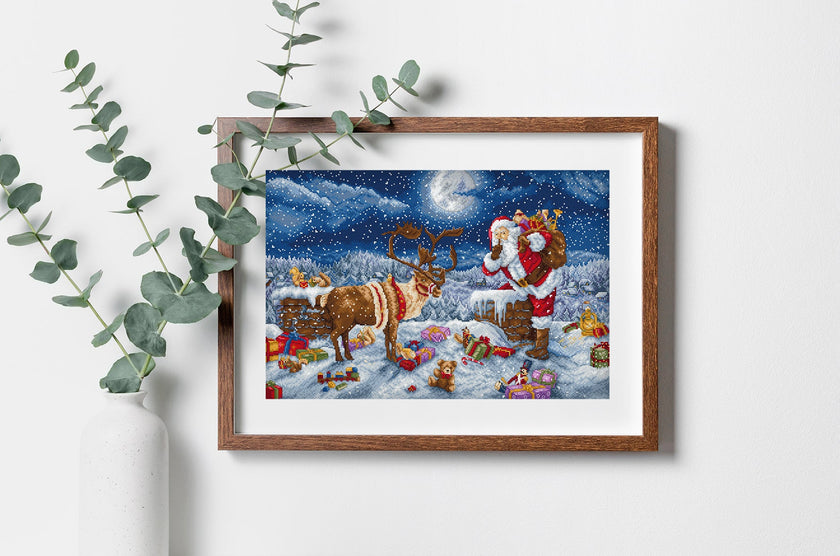 Framed artwork of Santa Claus and reindeer with Christmas scene, surrounded by eucalyptus leaves.