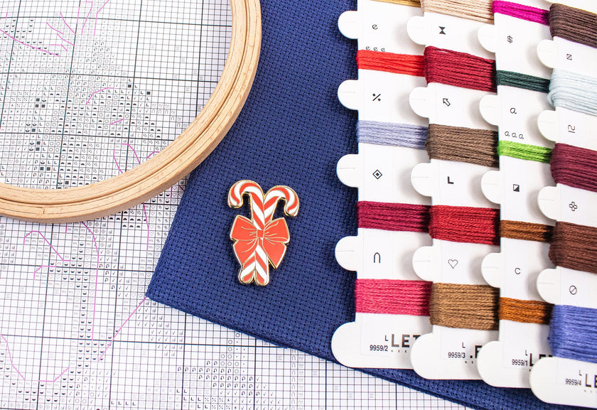 Embroidery hoop, colorful thread spools, and a candy cane ornament on a grid background