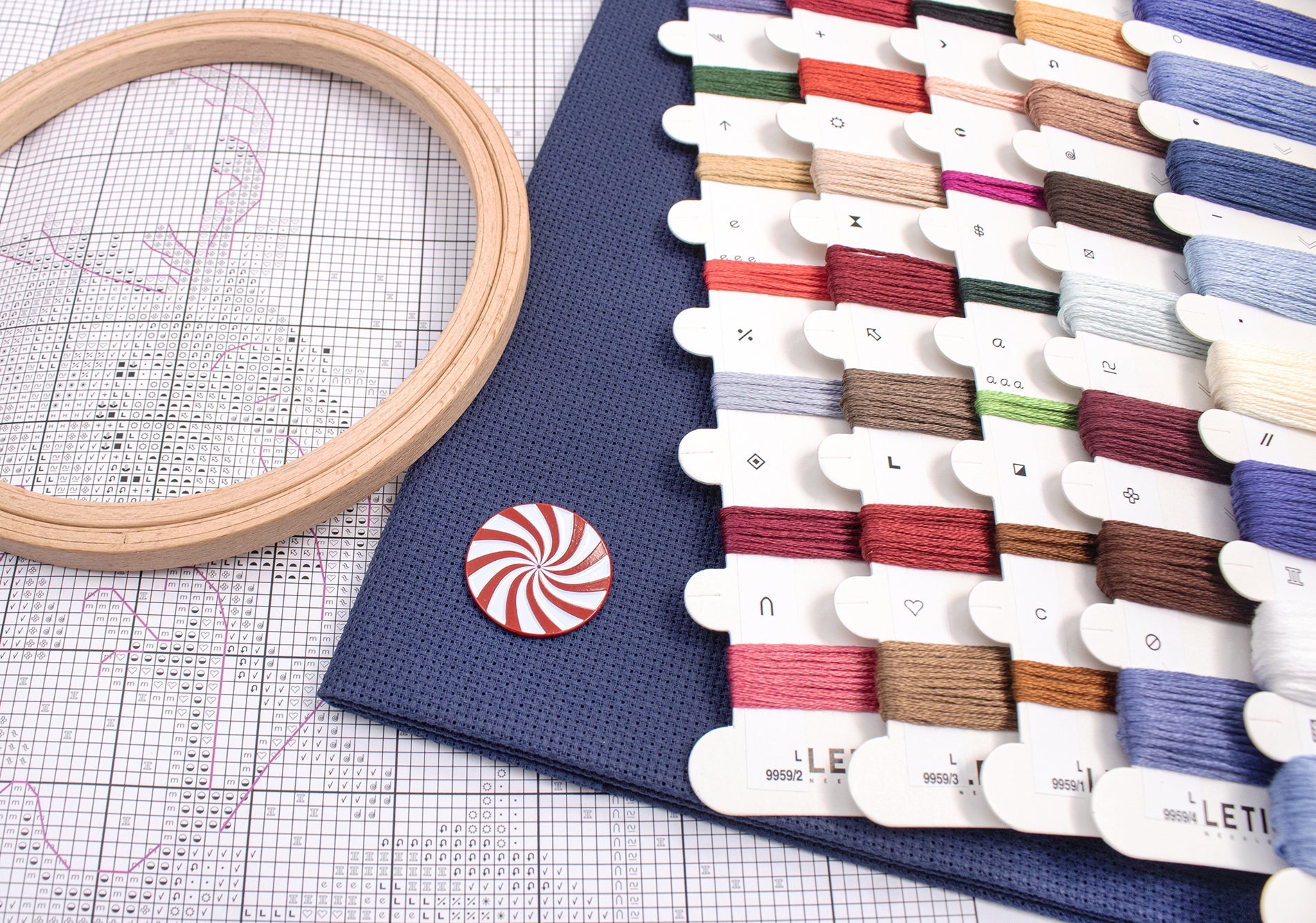 Embroidery hoop and thread spools on a grid surface with a brand mat.