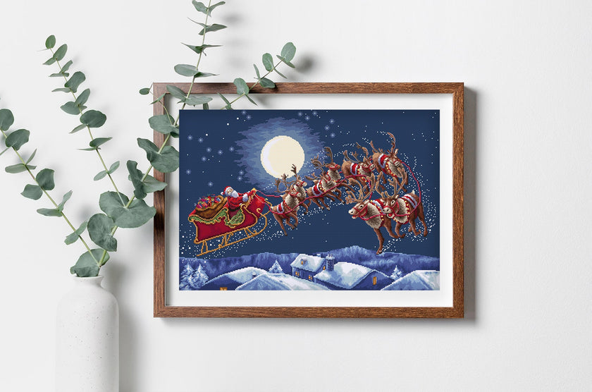 Framed artwork of Santa Claus in a sleigh with reindeer against a night sky with a full moon.