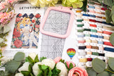 Embroidery kit with a pink frame, pattern book, and thread spools on a floral background
