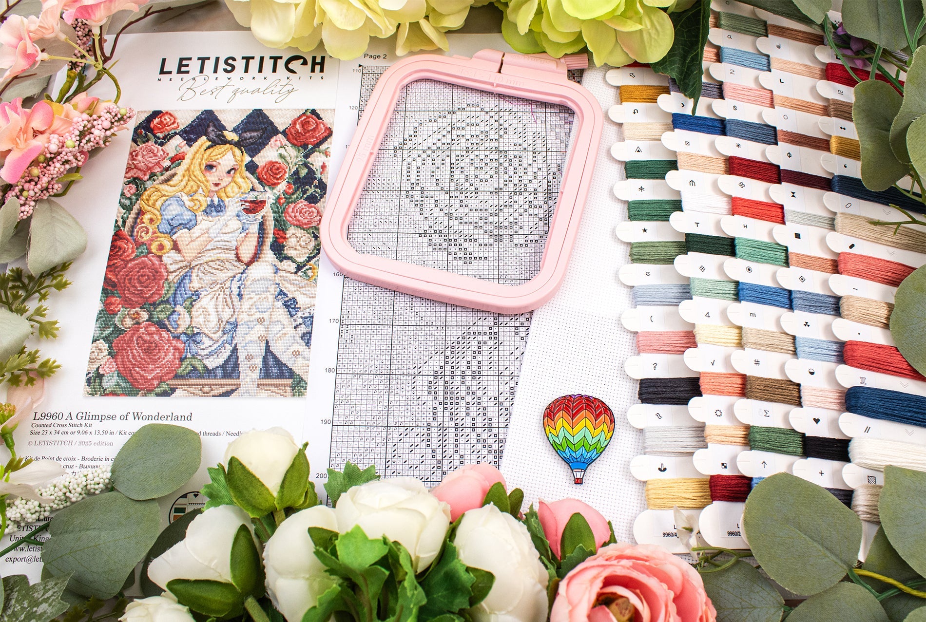 Embroidery kit with a pink frame, pattern book, and thread spools on a floral background