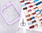 Embroidery hoop, scissors, and thread spools on a white surface with grid pattern