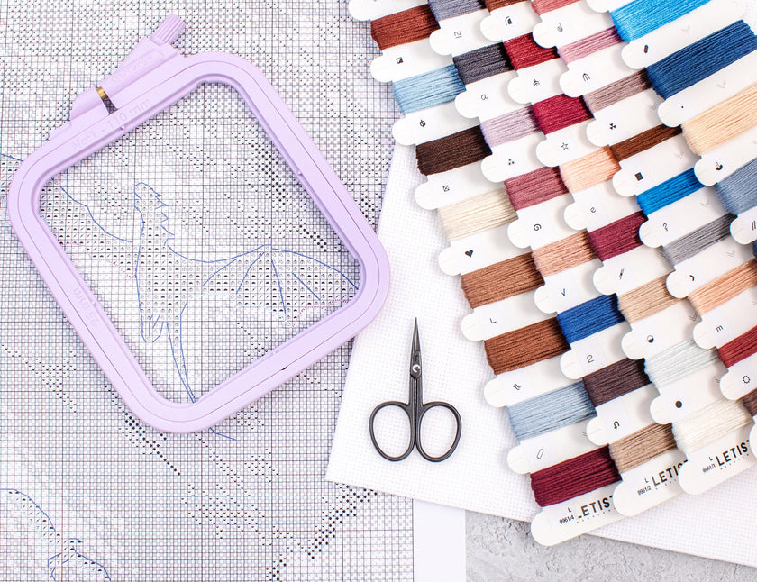Embroidery hoop, scissors, and thread spools on a white surface with grid pattern