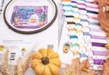 Embroidery hoop with a pumpkin-themed design, colorful thread spools, and pumpkins on a table.