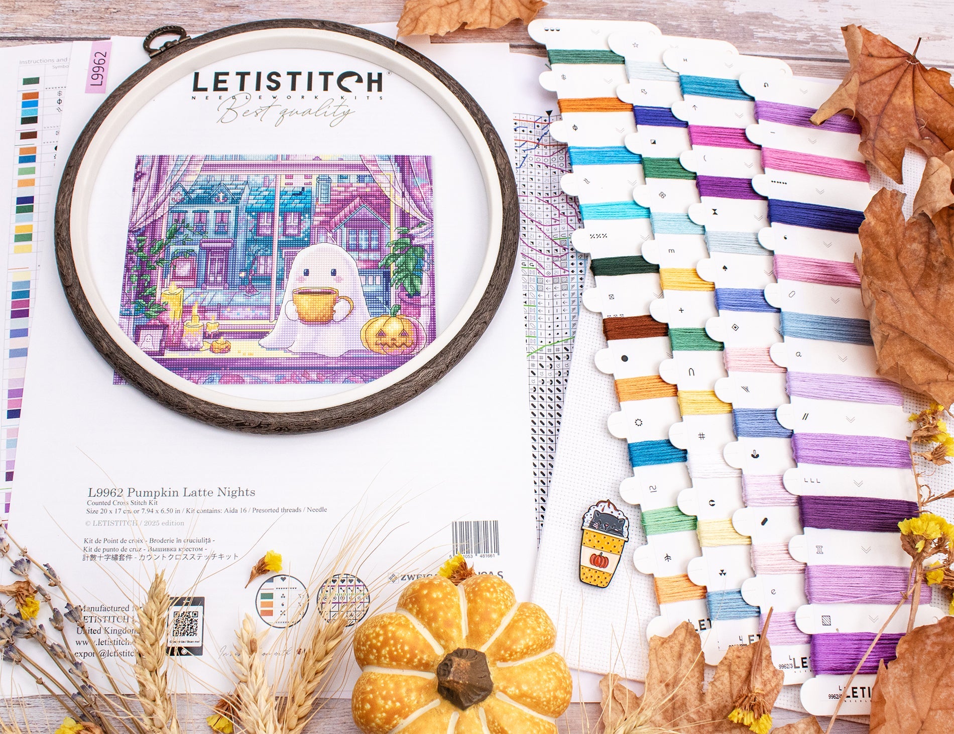 Cross-stitch hoop with a pumpkin-themed design, surrounded by colorful threads and autumn decorations.