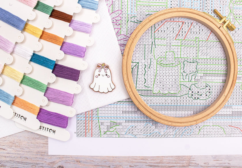 Embroidery hoop with cross-stitch pattern and colorful threads on a wooden surface