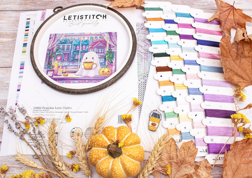 Embroidery hoop with a colorful design, surrounded by threads and autumn decorations on a wooden surface.