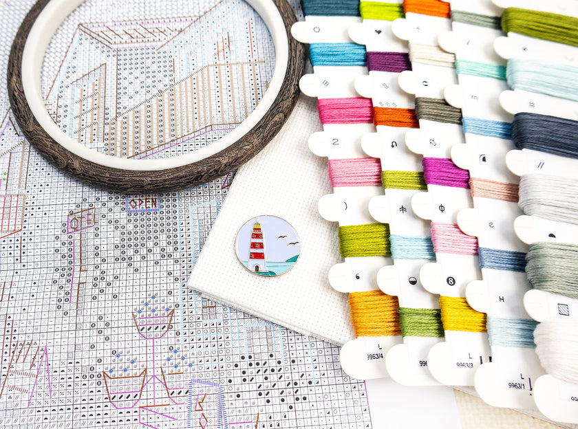 Embroidery hoop, thread spools, and cross-stitch pattern on a white surface