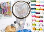 Embroidery hoop with a partially completed design, colorful threads, and seashells on a table.