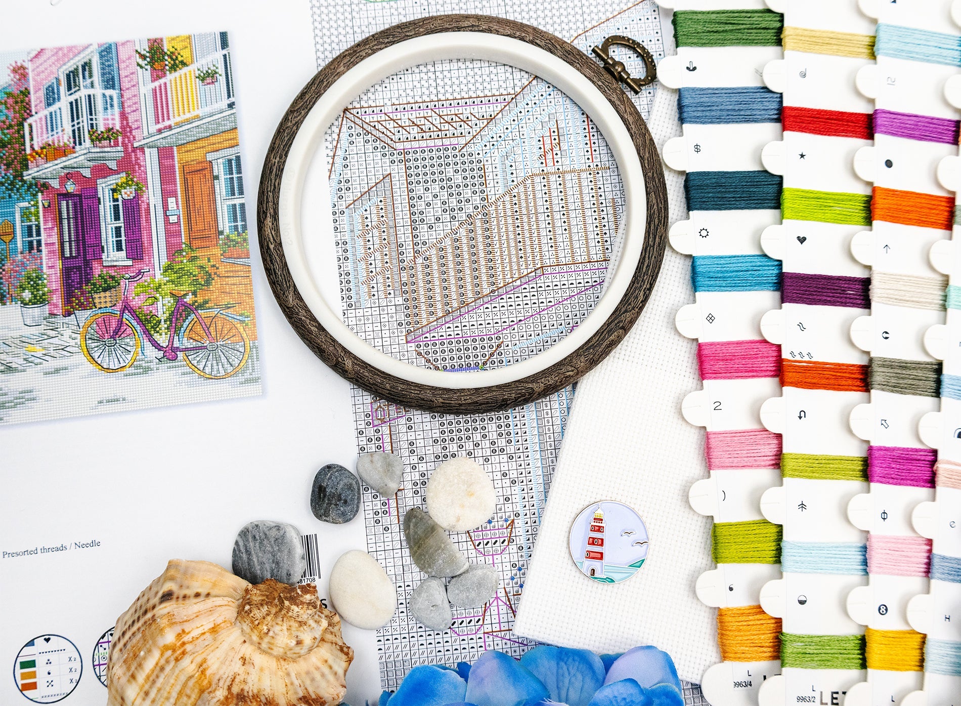 Embroidery hoop with a partially completed design, colorful threads, and seashells on a table.